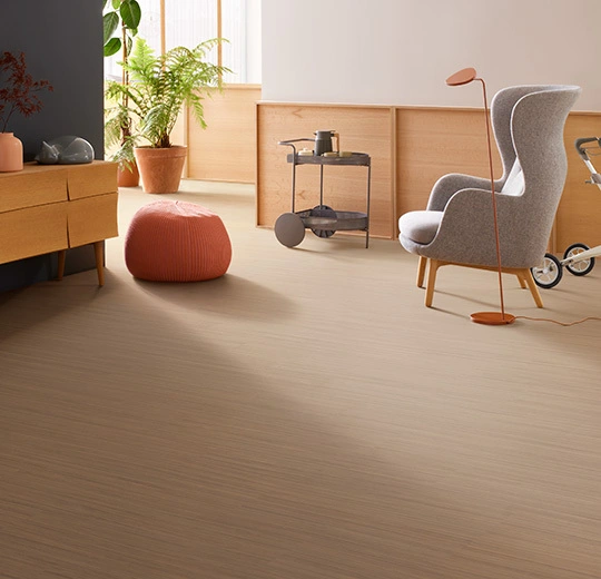 Modern lounge space with smooth beige linoleum flooring, a grey wingback armchair, and warm wood furniture.