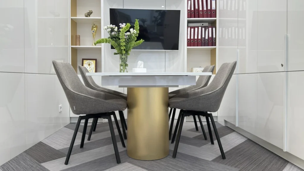 Sleek office meeting area featuring grey chevron-patterned carpet tiles, a brass pedestal table, and white built-in cabinets.