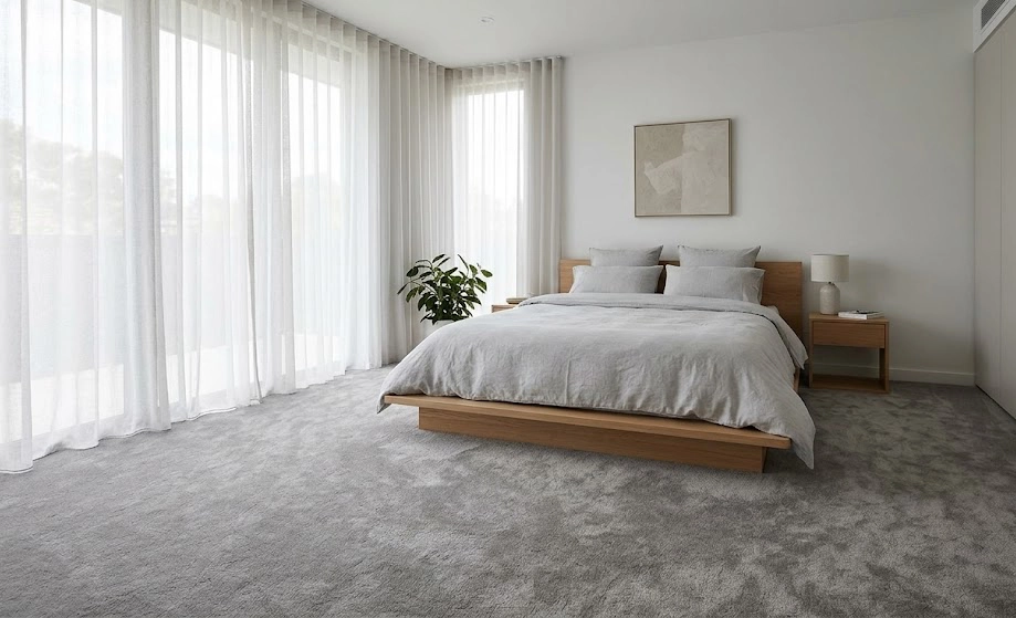 Minimalist bedroom with plush grey carpet, platform bed, and floor-to-ceiling windows.